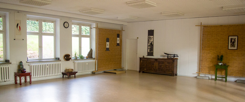 Heller Übungsraum der Tai-Chi-Schule mit Holzboden, Bambusmatten und chinesischen Schriftrollen an den Wänden